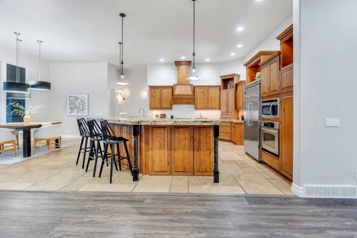 Kitchen featuring a large island with a stone-finish countertop, wood cabinetry, stainless steel appliances, recessed lighting, and tile flooring