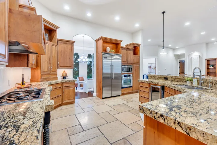 Kitchen with light wood cabinetry, stone countertops, stainless steel appliances, a gas range, and stone tile flooring