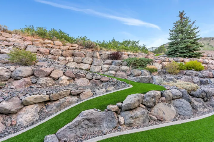 Landscaped retaining wall system with natural stone boulders and integrated artificial turf pathways