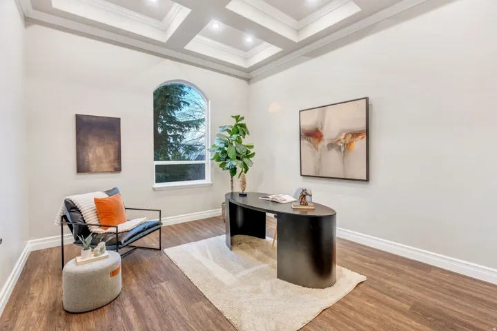Spacious room featuring wood-finish flooring, a coffered ceiling with recessed lighting, an arched window, and white baseboards