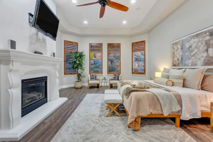Spacious room featuring a white fireplace with an ornate mantel, wood-finish flooring, and a tray ceiling with recessed lighting