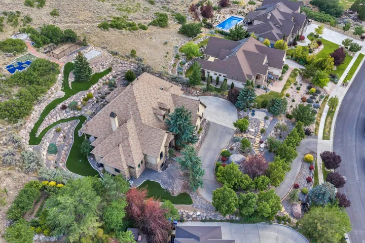Expansive property featuring a stone and stucco exterior, a multi-car driveway, mature landscaping, a sports court, and an artificial turf putting green