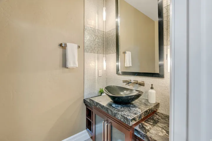 Modern vanity with a dark vessel sink, stone countertop, built-in cabinetry, and wall-mounted faucet