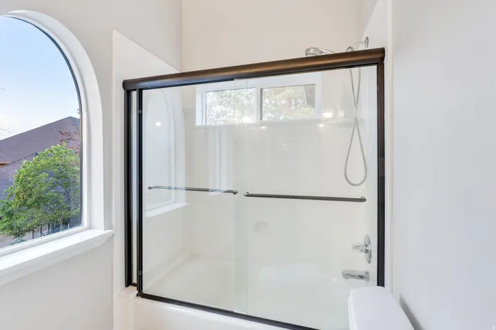 Bathtub with a sliding glass enclosure, arched window, and additional transom window
