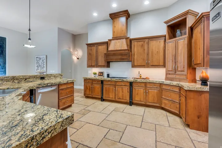 Spacious kitchen featuring custom wood cabinetry, granite countertops, stone tile flooring, and stainless steel appliances