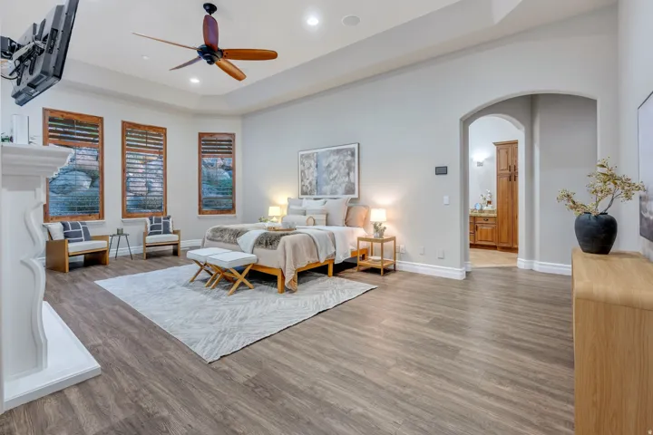 Spacious bedroom featuring wood-finish flooring, a recessed ceiling with a ceiling fan, and a bay window with plantation shutters
