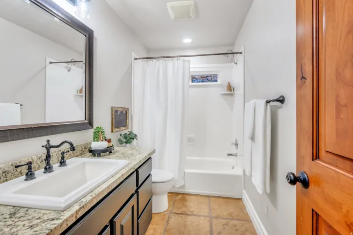 Bathroom with a dark wood vanity, light speckled countertop, and rectangular undermount sink with a dark bronze faucet