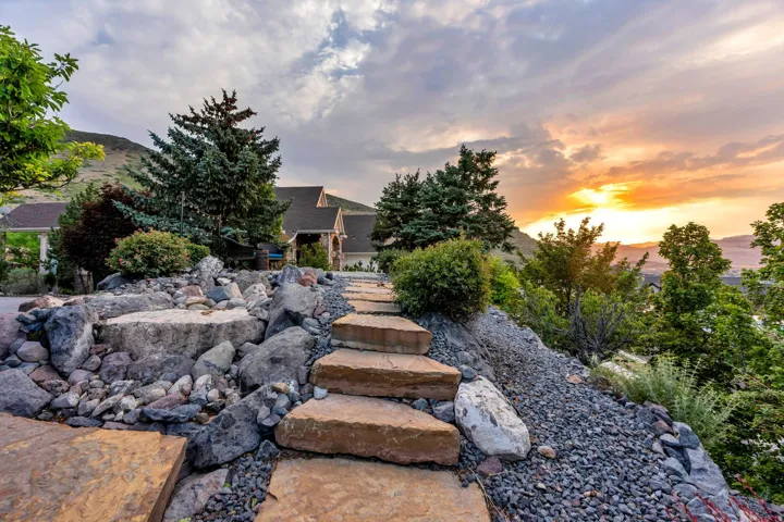 Natural stone pathway with large flagstone steps, surrounded by extensive rock landscaping and mature evergreen trees
