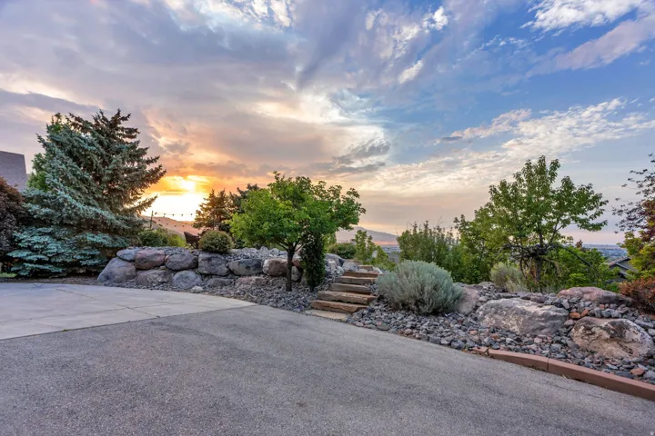 Paved driveway with a stone retaining wall, mature trees, and a terraced landscape featuring stone steps