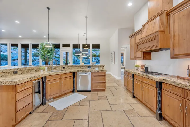 Gourmet kitchen featuring stone tile flooring, granite countertops, wood cabinetry, stainless steel appliances, and a built-in beverage cooler