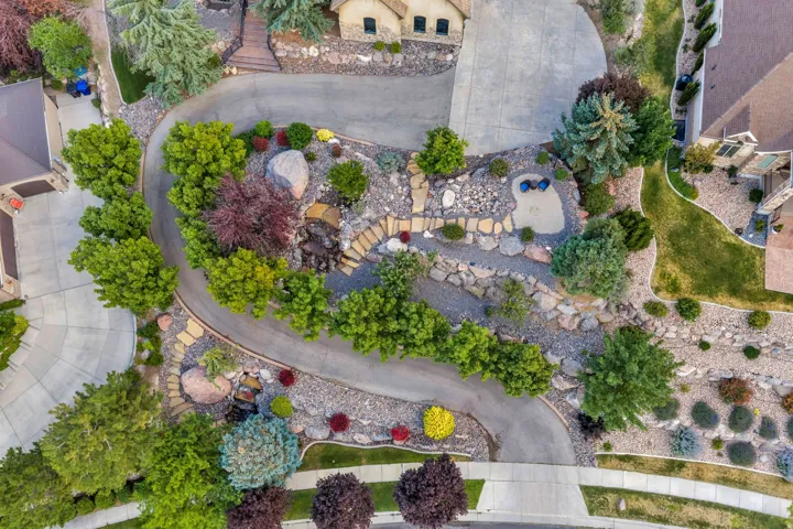 Curving driveway leading to a multi-level rock garden with diverse plantings, stone steps, and a decorative water feature