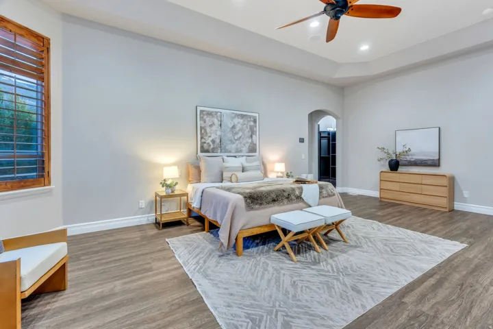 Spacious interior featuring wood-finish flooring, a tray ceiling with a ceiling fan, recessed lighting, and a large window with wood plantation shutters