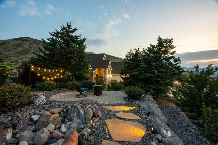 Expansive outdoor patio area featuring a gravel surface, string lighting, and integrated landscape boulders