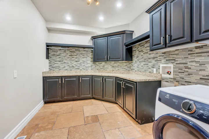 Utility room featuring extensive dark cabinetry, light-toned countertop space, a mosaic tile backsplash, and large format floor tiles