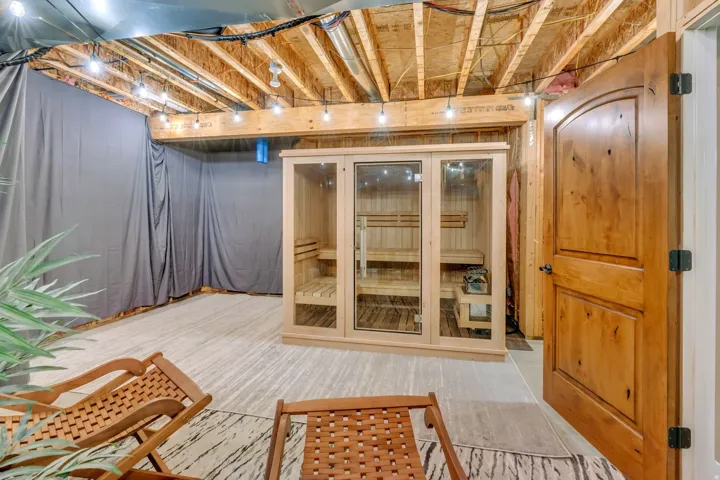 Dedicated sauna room featuring a glass-front cedar sauna, exposed wood beam ceiling, and string lighting