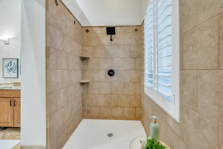 Walk-in shower with tiled walls, built-in shelving, matte black fixtures, and an integrated window with white plantation shutters