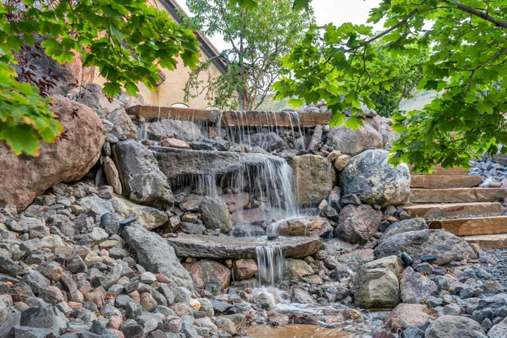 Multi-tiered rock waterfall feature with natural stone steps and surrounding foliage