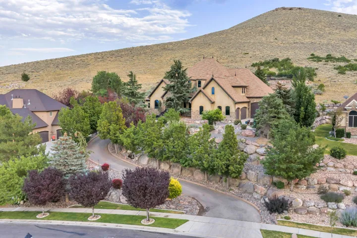 Grand custom residence nestled into a hillside, featuring a distinct architectural style with multiple gables and arched window details