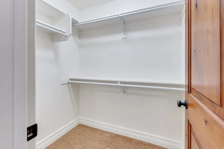 Walk-in closet featuring built-in shelving, dual hanging rods, light-colored carpet flooring, and white trim