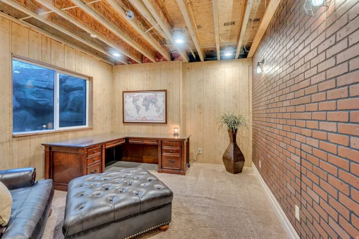 Exposed ceiling joists with recessed lighting, complemented by a brick accent wall and light-toned vertical wood paneling