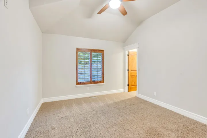 Carpeted room featuring a vaulted ceiling and a ceiling fan with light fixture