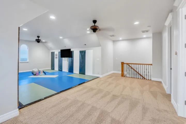 Versatile bonus room featuring a dedicated area with blue and green mats, wall-mounted television, and a distinctive arched window
