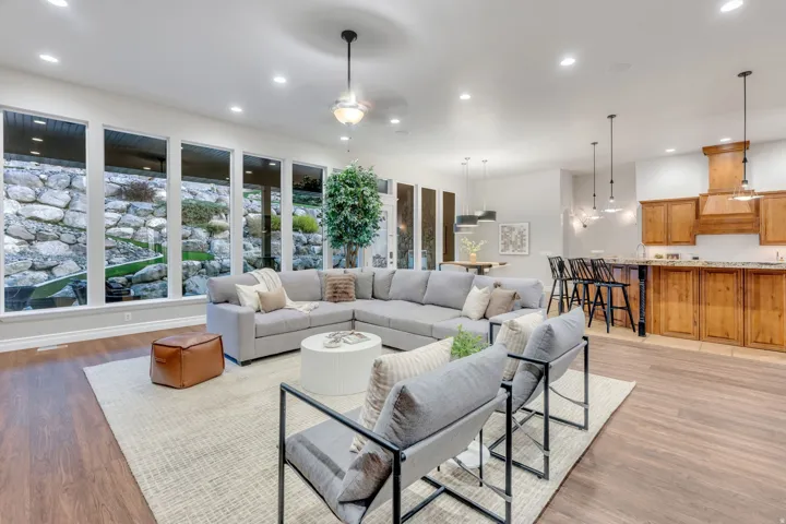 Open-concept living area featuring wood-finish flooring, a wall of five vertical windows, recessed lighting, and a kitchen with wood cabinetry, a custom range hood, and a bar-height counter
