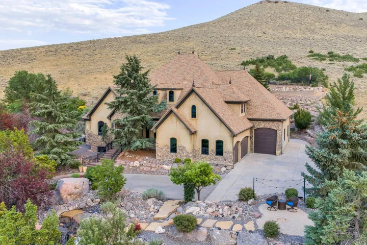 Exterior of a stucco and stone residence featuring a multi-car garage, pitched shingle roof, arched windows, and a stone retaining wall