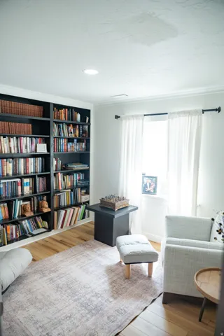 Built-in shelving unit with crown molding, natural wood-finish flooring, recessed lighting, and a window with a dark-finish curtain rod