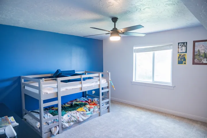 Carpeted room featuring a ceiling fan with integrated lighting, a single window with blinds, and a blue accent wall
