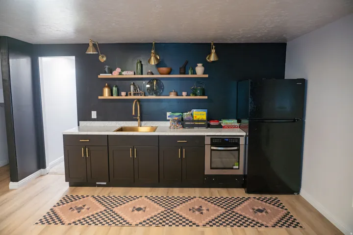 Kitchenette featuring dark cabinetry, light countertops, and a gold-finish sink and faucet