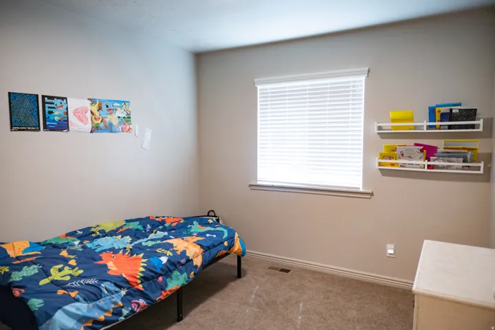 Carpeted room featuring a single window with blinds, base molding, and built-in wall shelving