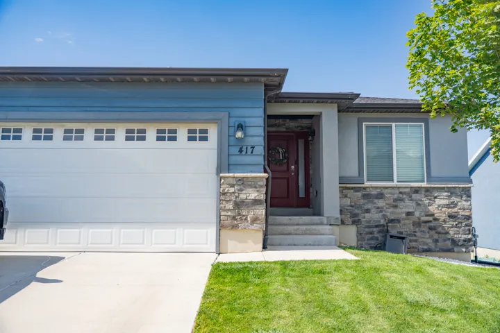 Contemporary facade featuring a blue siding, a red entry door, a white garage door with upper window panels, and a stone veneer foundation