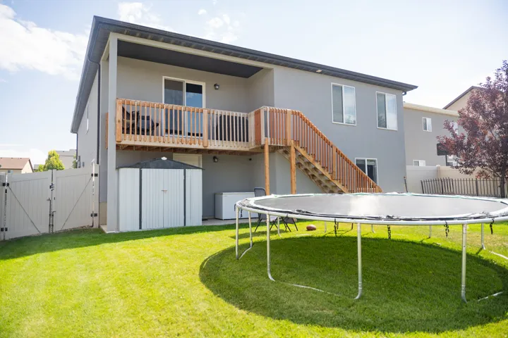 Expansive backyard featuring a manicured lawn, full fencing, a ground-level patio, a second-story deck with wooden railing and stairs, and an exterior storage shed
