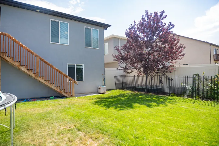 Private backyard featuring a well-maintained lawn, a mature deciduous tree, and a PVC privacy fence