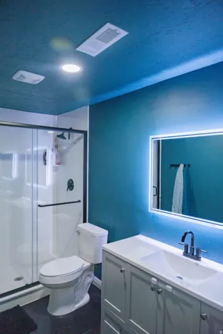 Contemporary bathroom featuring a walk-in shower with clear glass enclosure, a vanity with integrated sink and storage, a back-lit mirror, and recessed ceiling lighting