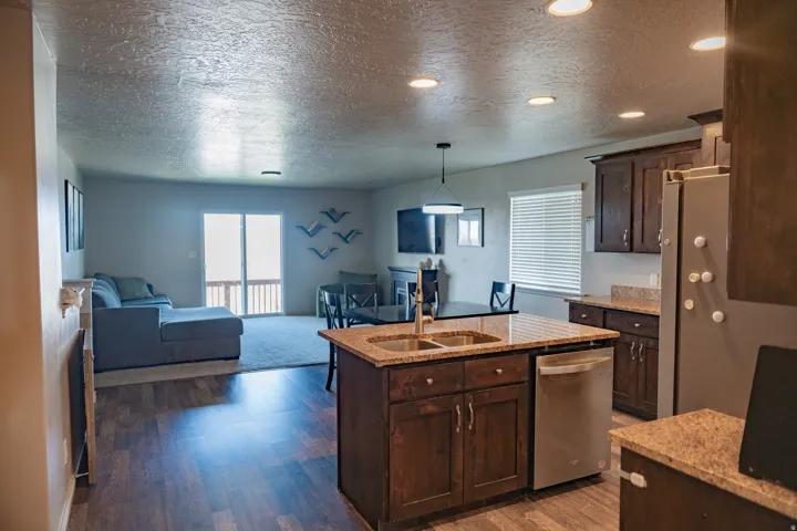 Open-concept living space with wood-finish flooring, recessed lighting, and a kitchen island featuring a double-basin sink
