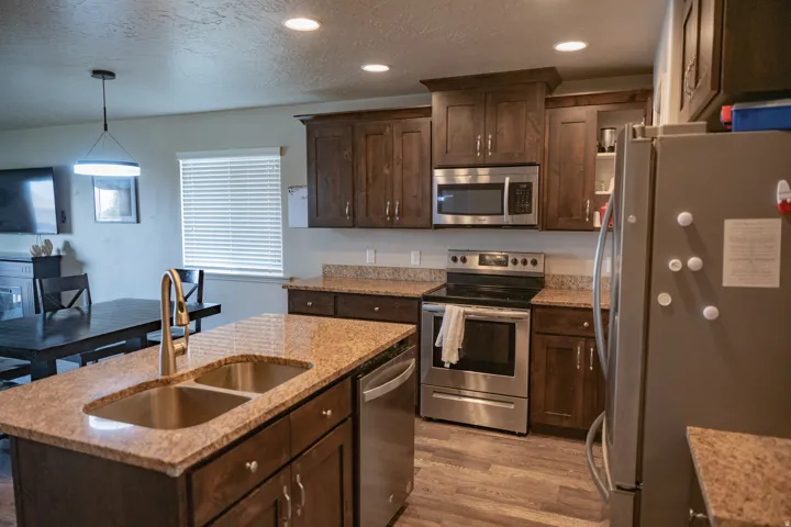 Kitchen featuring wood-finish flooring, granite-style countertops, stainless steel appliances, dark wood cabinetry, and recessed lighting