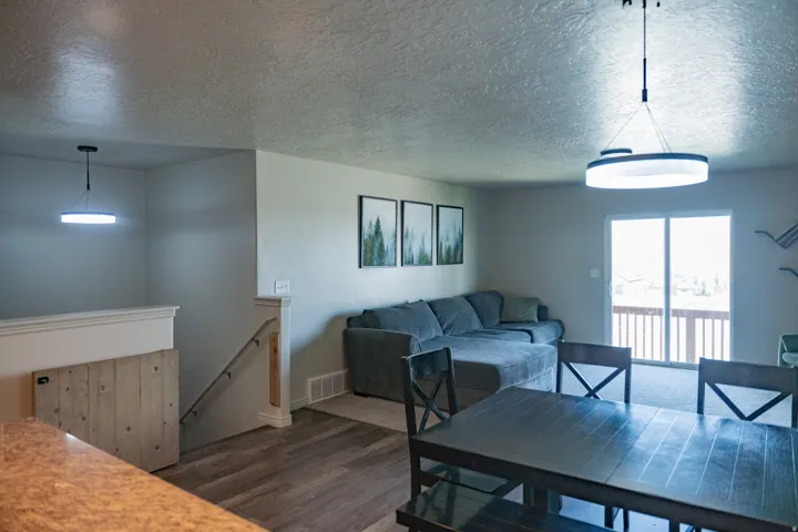 Open-concept living area featuring wood-finish flooring, a sliding glass door to an exterior deck, and contemporary pendant lighting fixtures