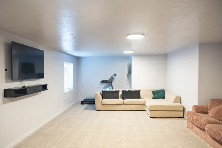 Spacious room featuring light-toned carpeting, a wall-mounted television, a floating media console, and recessed lighting