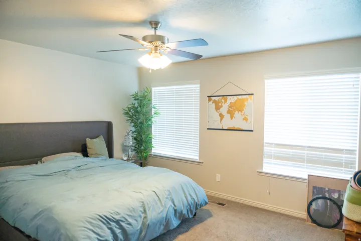 Bedroom featuring neutral-toned walls, carpeted flooring, two windows with blinds, and a ceiling fan with integrated lighting