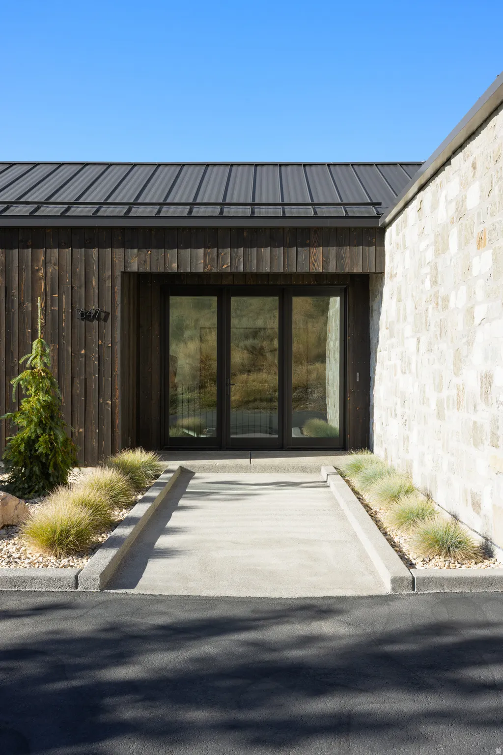 Modern exterior featuring a dark metal standing seam roof, vertical wood siding, and stone facade