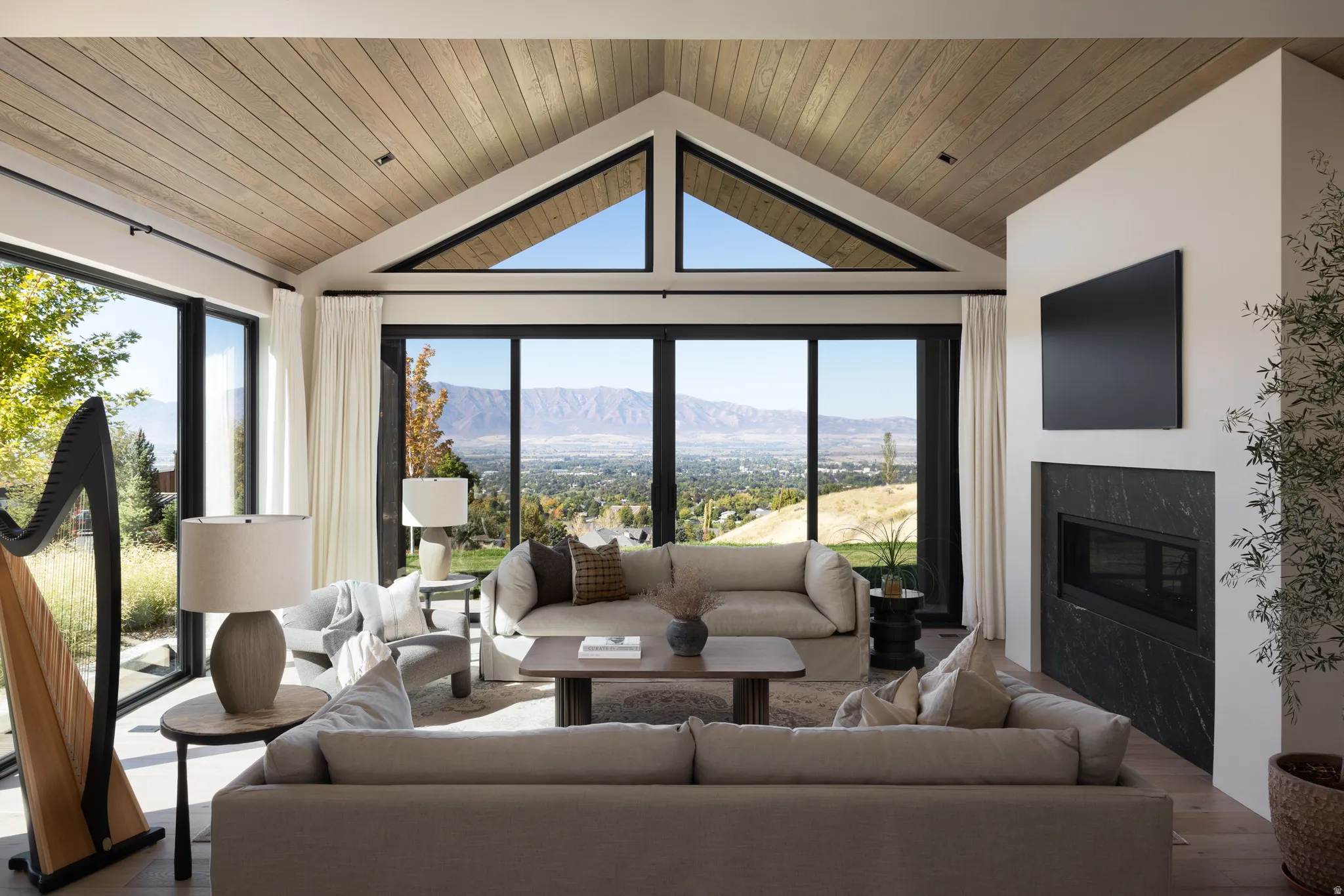 Vaulted wood-paneled ceiling with exposed beams, expansive floor-to-ceiling windows, and a built-in linear fireplace with a dark stone surround