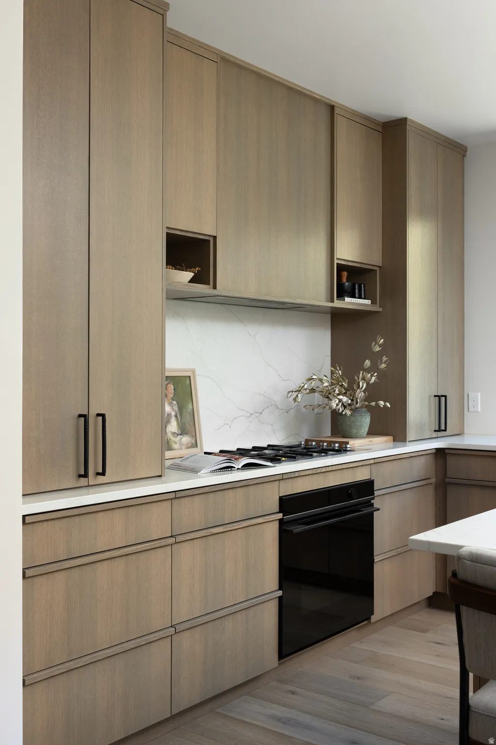 Modern kitchen featuring light wood-finish cabinetry with black hardware, white countertops, and a white veined backsplash