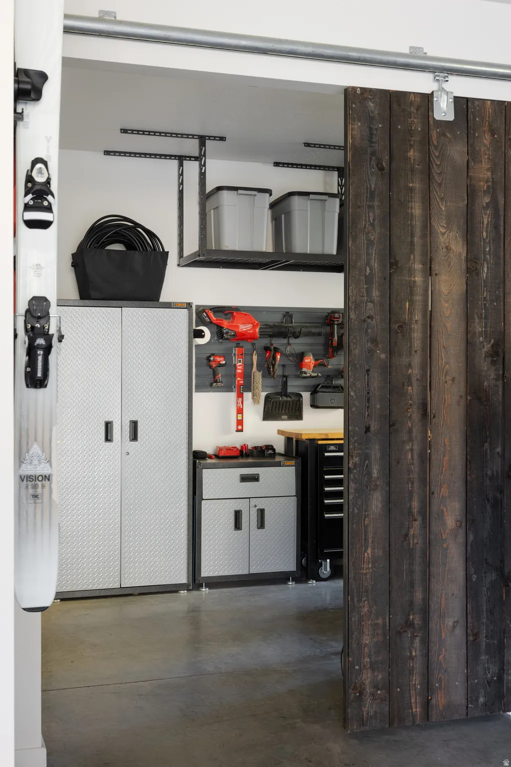 Garage featuring a barn door entry, concrete flooring, overhead storage racks, metal cabinetry, and a wall-mounted tool organization system