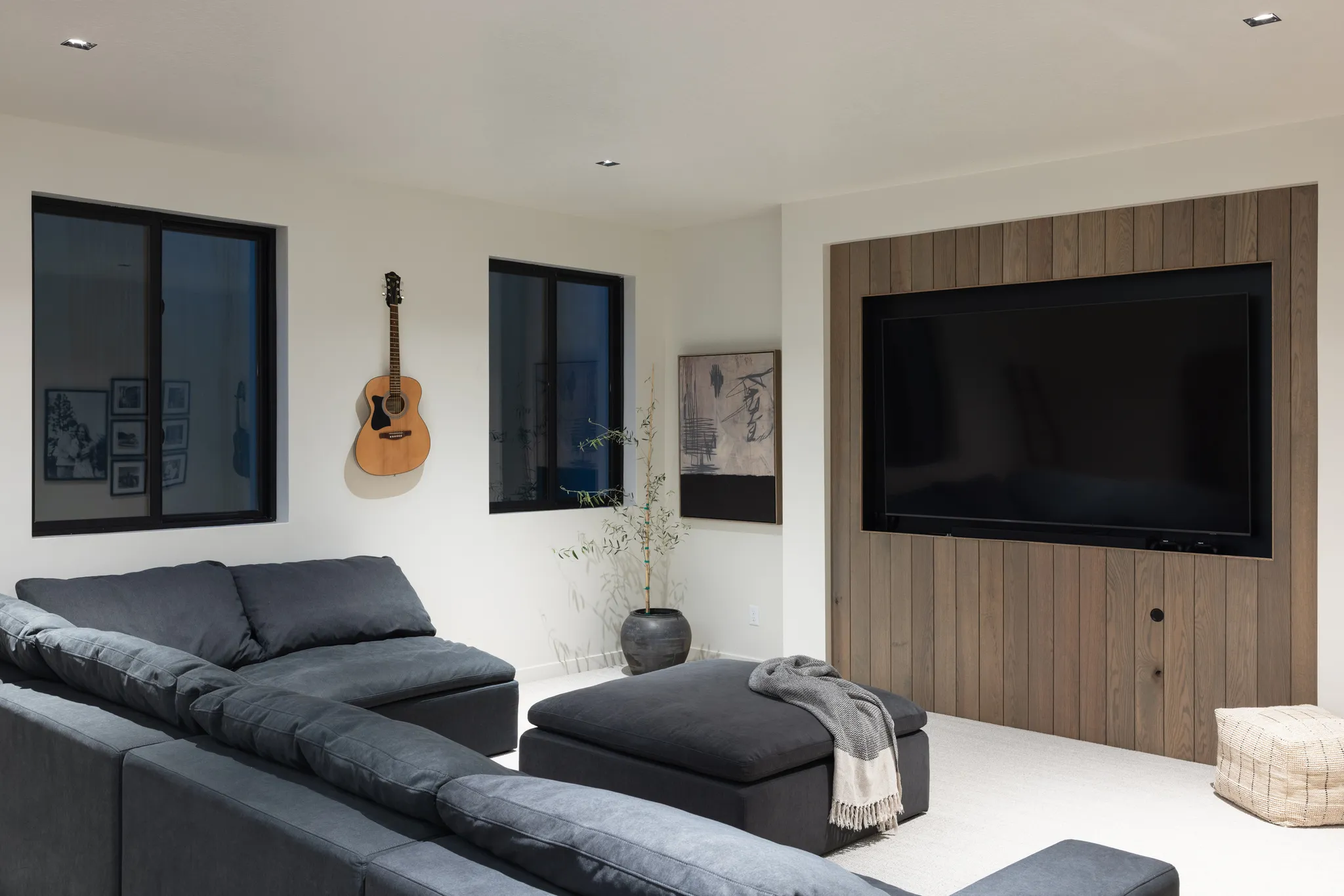 Recessed television with wood-paneled feature wall, two windows with dark frames, light-colored flooring, and ceiling-mounted lighting fixtures