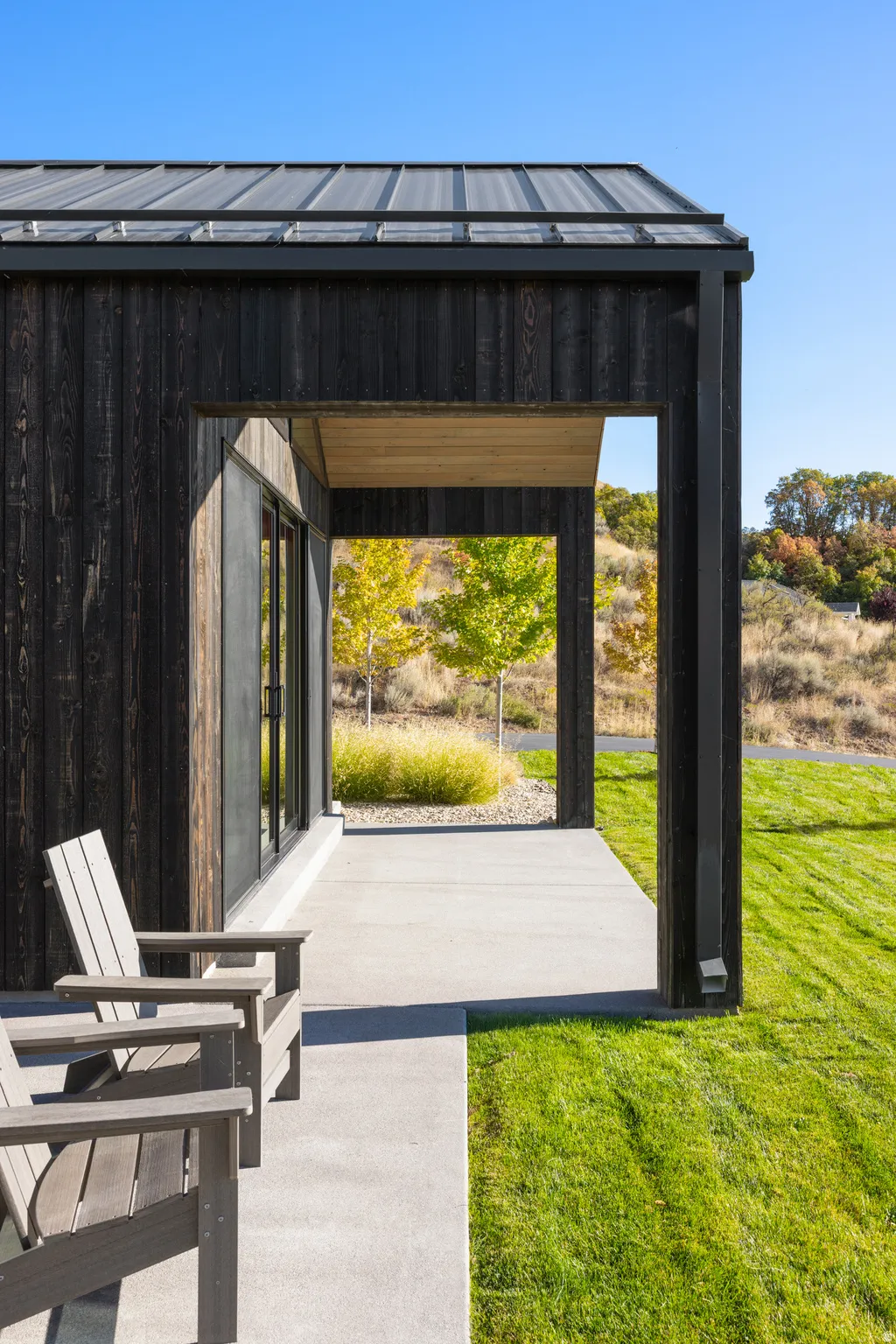 Modern exterior featuring dark vertical siding, a standing seam metal roof, and a covered concrete patio