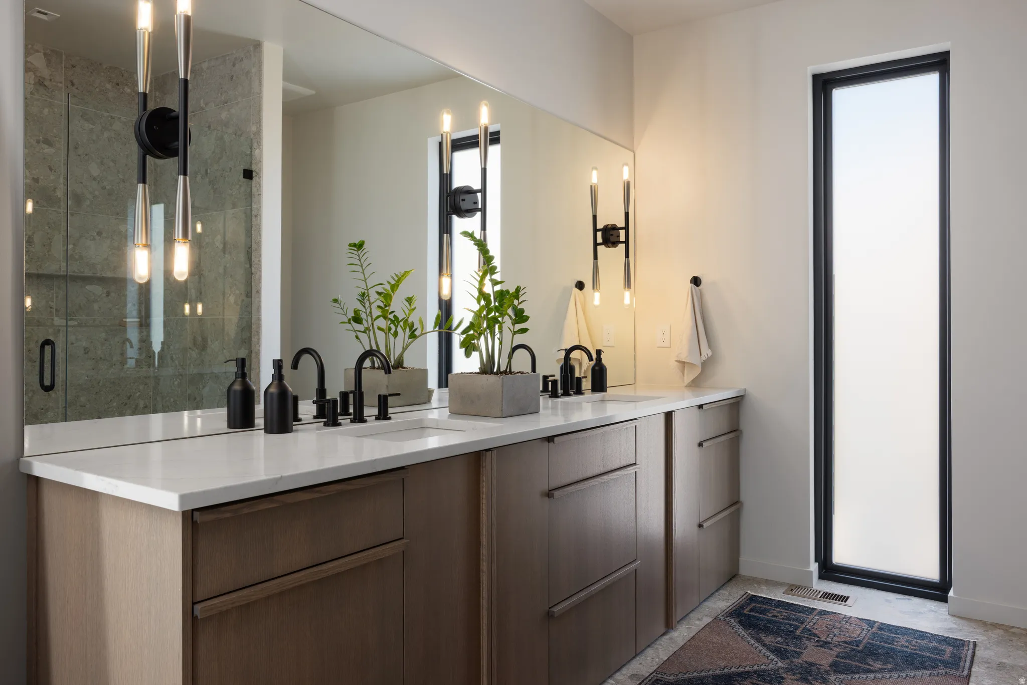Dual vanity featuring light wood-finish cabinetry, white stone countertops, and matte black fixtures