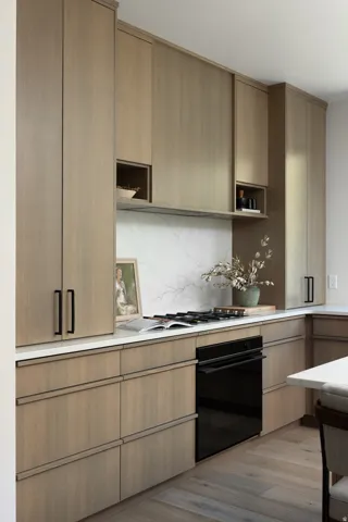 Modern kitchen featuring light wood-finish cabinetry with black hardware, white countertops, and a white veined backsplash