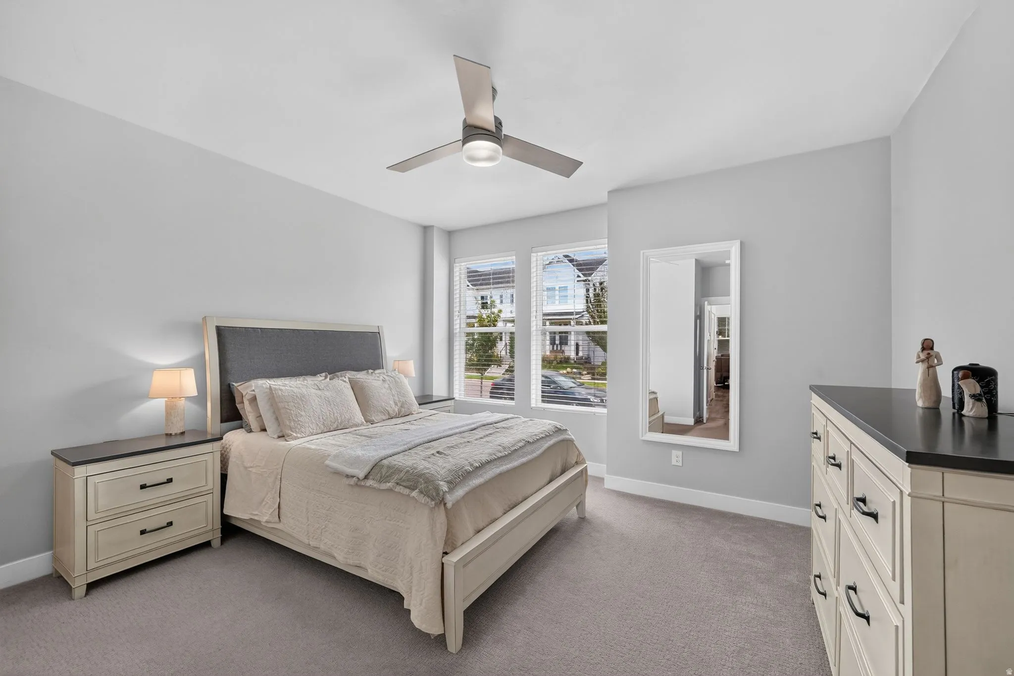 Spacious bedroom featuring light gray carpeting, a large window with white trim, and a contemporary ceiling fan